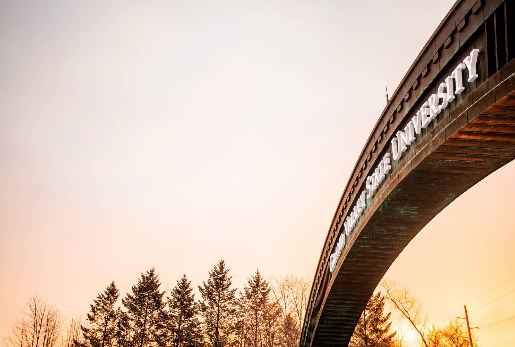 The Grand Valley State University Arch off Lake Michigan Drive that leads into north campus is pictured at sunrise. The sky is pink and orange.